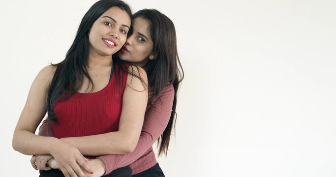 Two beautiful girlfriends from India hugging with a white background