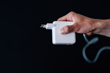 Closeup shot of a hand holding a power adapter on a black background