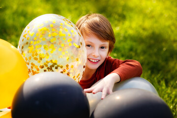 Cute charming red-haired boy with colorful balloons in an open park. The kid is enjoying the game. Happy birthday, festive celebration.