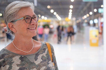 Side view of an elderly woman enjoying shopping in a mall, smiling looking at a shop window. Happy gray haired people