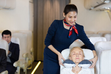 flight attendant or air hostess giving a pillow to senior woman when sleeping during a flight