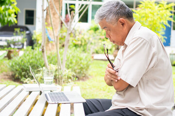 Portrait of old elderly Asian man using a computer laptop in the backyard for learning new skill...