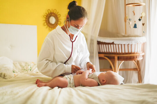 Doctor nurse listens with a stethoscope to baby child at home in bedroom, examination of baby at home, patronage. Regular medical check-ups for babies