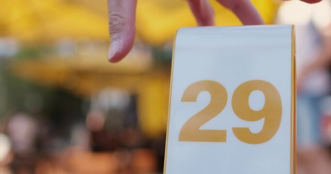 A man's hand removes from the video a stand with an order number in a cafee, tables and people out of focus in the background.