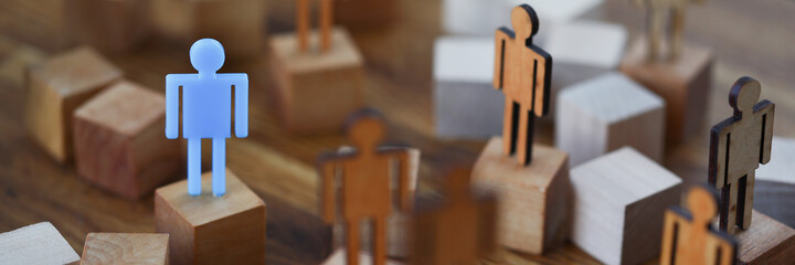 Wooden men on wooden cubes of brown color, one of them is blue