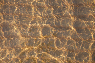 Fototapeta na wymiar View through the water and waves on the sand with sunlight, abstract natural background