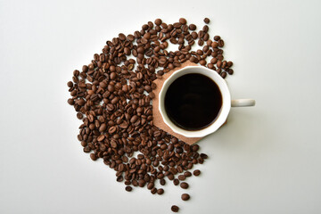 Coffee in a cup and scattered coffee beans on a white background, top view