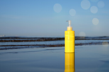 Sunbath lotion sun protection in yellow plastic bottle on sea background with bokeh, copy space