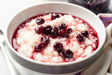 Rice pudding or porridge with cherry jam in bowl on concrete background