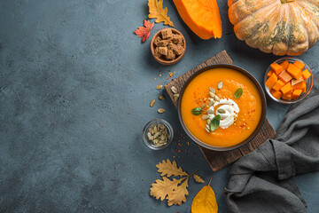 Healthy, autumn pumpkin cream soup with cream and basil on a dark blue background with autumn...