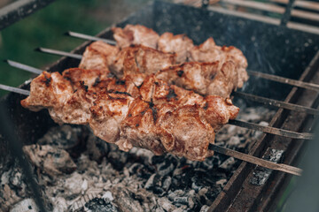 Raw grilled meat on skewers is cooked on charcoal grill, cooking barbecue outdoors
