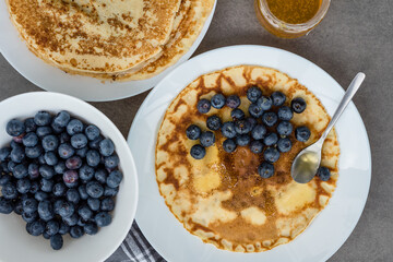 Pancakes, blueberries and honey on a white table on a gray concrete background. Maslenitsa concept and summer time. 