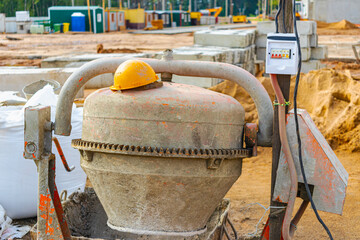 An industrial concrete mixer at a construction site with an orange worker's helmet lying on it....