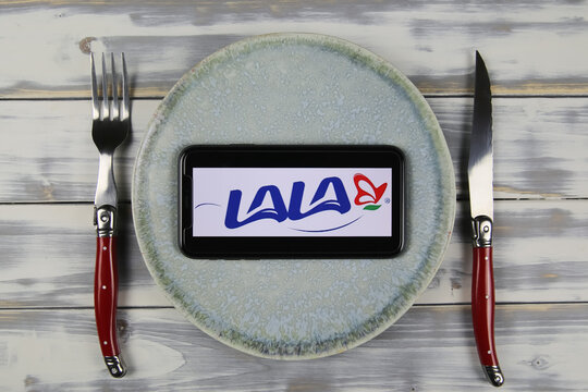 Viersen, Germany - May 9. 2021: Closeup of mobile phone on plate and wood table, cutlery with logo lettering of mexican lala grupo dairy company (focus on center)