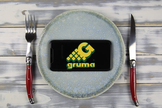 Viersen, Germany - May 9. 2021: Closeup of mobile phone on plate and wood table, cutlery with logo lettering of mexican gruma food company (focus on center)