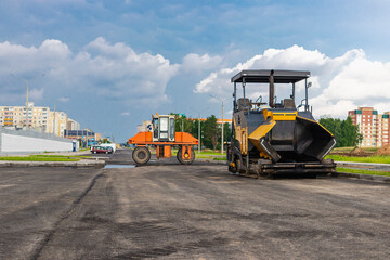 Fototapeta na wymiar Asphalt paving equipment. Asphalt paver and heavy vibratory roller. Construction of new roads and road junctions. Heavy construction industrial machinery.