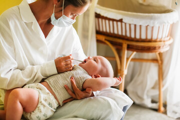 Doctor nurse examines the throat of the baby's child at home in the bedroom, examining the baby at home, patronage. Regular medical examination of babies, preventive examination, family doctor