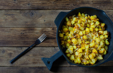 Fried potatoes and onion in a pan on black background