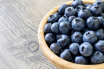 Fresh blueberries in a bamboo bowl on a wooden table close up. Healthy diet high in antioxidants concept. Highly detailed half bowl view with natural light and copy space.