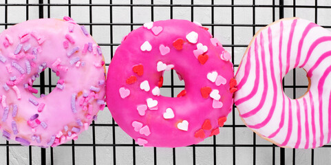 Three pink donuts with different icings and sprinkles on cooling rack on the white table. American dessert. Top view