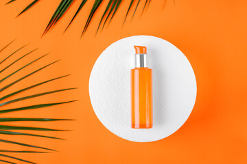 Orange dispenser bottle on white podium on orange. Skincare product. Unlabeled container. Flat lay
