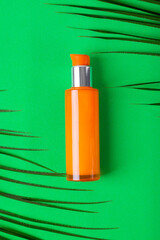 Orange dispenser bottle on green background with palm leaves. Organic skincare product. Unlabeled container