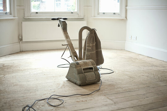 Floor sander standing on freshly sanded floorboards in empty living room