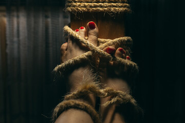 Female feet with red nail polish tied to the wooden beam with shabby rope