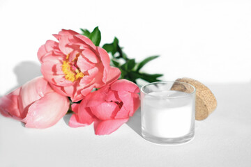 Fototapeta na wymiar white scented candle and red peony flowers. home fragrances for cozy atmosphere. flower fragrance for home. unbranded ceramic candle.