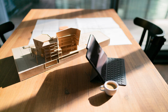 Laptop with coffee cup and architectural model on table at office