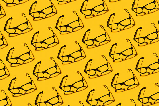 Pattern of rows of simple classic eyeglasses flat laid against yellow background