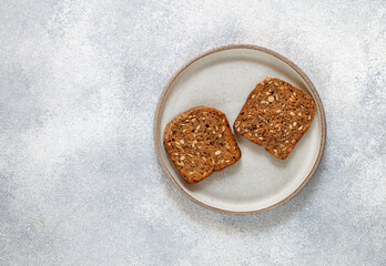 Two slices of rye whole-grain bread with sunflower seeds, flax and pumpkin on a gray plate on a light concrete background. Top view and copy space. Selective focus