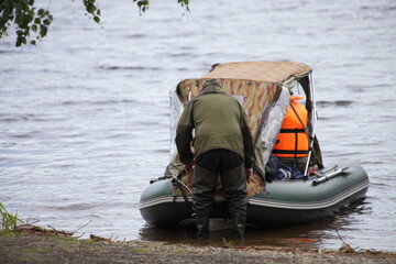 Fisher man pushes the awning inflatable boat away from the shore in the water, fishing recreation...