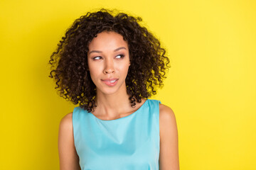 Photo of dreamy minded young dark skin woman look empty space bite lips isolated on yellow color...