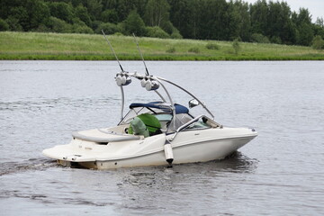 White motor boat with targa on river water on green grassy forest shore background at summer day,...