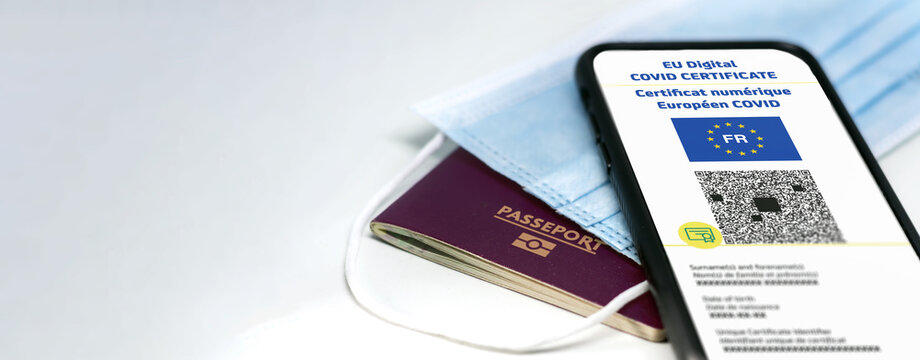 French EU Digital COVID Certificate with the QR code on the screen of a mobile phone over a surgical mask and a french passport