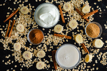 Cinnamon Roll Smoothie Ingredients on a Dark Wood Background: Almond milk, cinnamon, rolled oats, and other smoothie ingredients