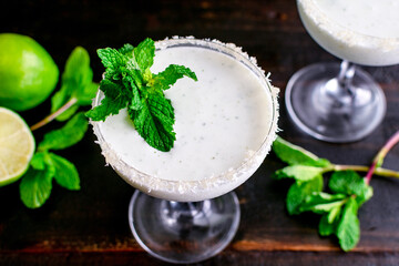 Coconut Mint Margaritas on a Dark Wood Background: Coconut and mint margaritas garnished with mint served in glasses rimmed with sugar and grated coconut