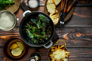Mussels in a pan, french fries, bread and beer on wooden rustic background, top view