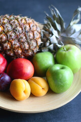 Wooden bowl with various colorful fruit on dark background. Selective focus.