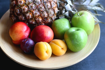 Wooden bowl with various colorful fruit on dark background. Selective focus.