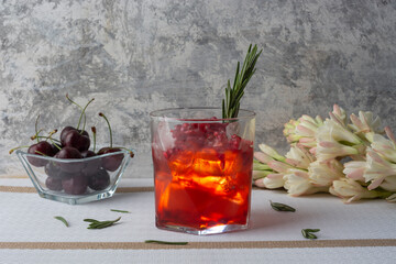 Bebida de arándano con hielos, granada y una rama de romero, acompañado de cerezas y flores