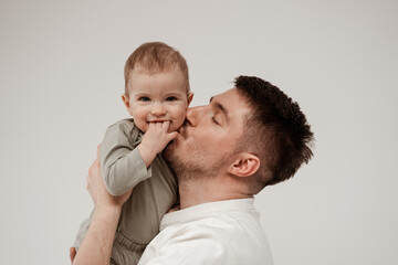 Young unshaven father kisses his little daughter on the cheek, the child smiles looking at the camera and holding three fingers in his mouth