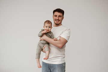 Young educator smiling, happy that he was able to calm the baby, looks into the camera holding the child in his arms, the child's teeth are cut, she holds her finger in her mouth and no longer crying