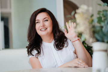 attractive woman in white clothes waving his hand at the table in a light room. 