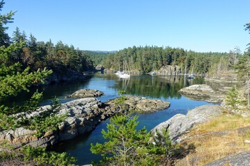 A view of a beautiful remote rocky cove surrounded by trees and pristine blue water, with boats...