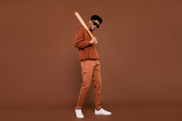 Full length profile side photo of young african man serious hold baseball bat isolated over brown...