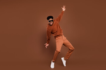 Fototapeta na wymiar Full length photo of funny short hairdo young guy dance dress spectacles sportswear trousers sneakers isolated on brown background