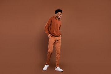 Full body photo of optimistic short hairdo young guy go dress sportswear trousers sneakers isolated on brown color background