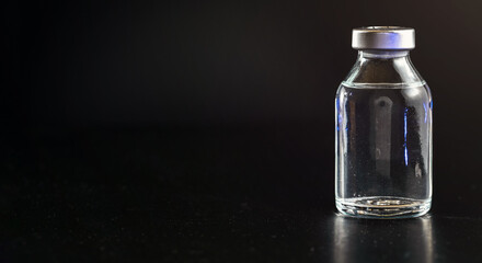 Clear vaccine bottle with no labels black background, space for text left side